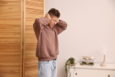 Photo of Annoyed young man covering his ears due to loud sound at home