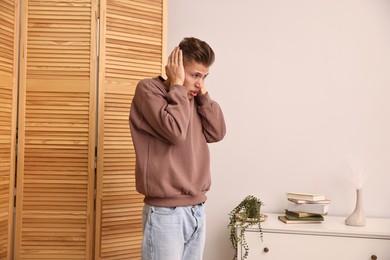 Photo of Annoyed young man covering his ears due to loud sound at home