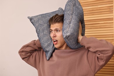 Annoyed young man covering his ears with pillows due to loud sound at home