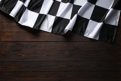 Photo of Checkered flag on wooden table, top view. Space for text