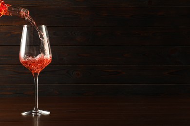 Photo of Pouring rose wine into glass at wooden table, space for text