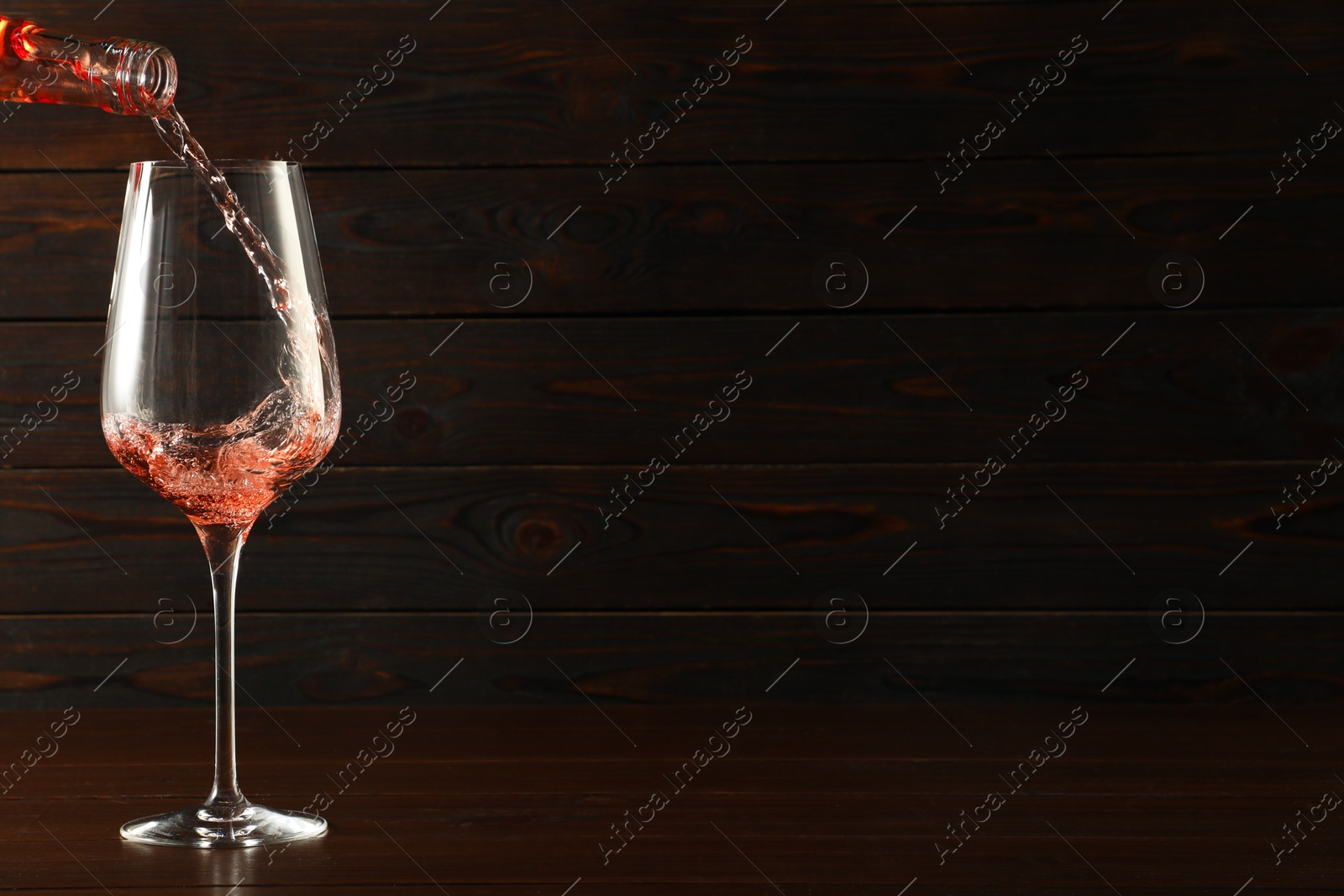 Photo of Pouring rose wine into glass at wooden table, space for text