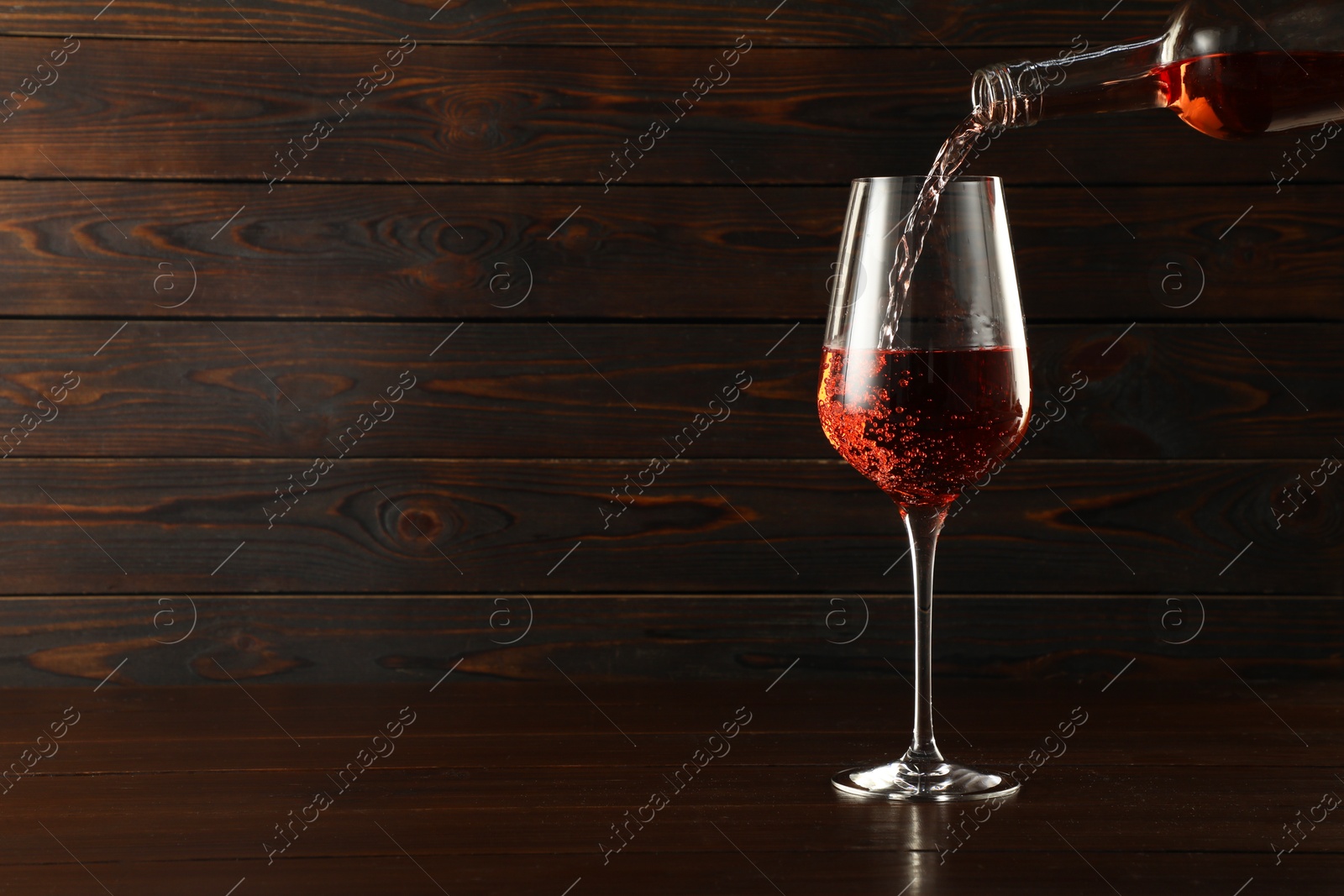 Photo of Pouring rose wine into glass at wooden table, space for text