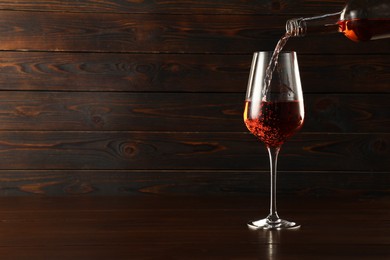 Photo of Pouring rose wine into glass at wooden table, space for text