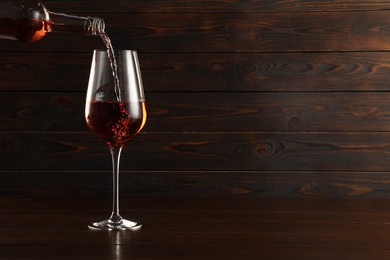 Photo of Pouring rose wine into glass at wooden table, space for text