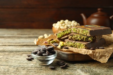 Photo of Pieces of Dubai chocolate bar with pistachios, knafeh and cacao chips on wooden table, closeup. Space for text