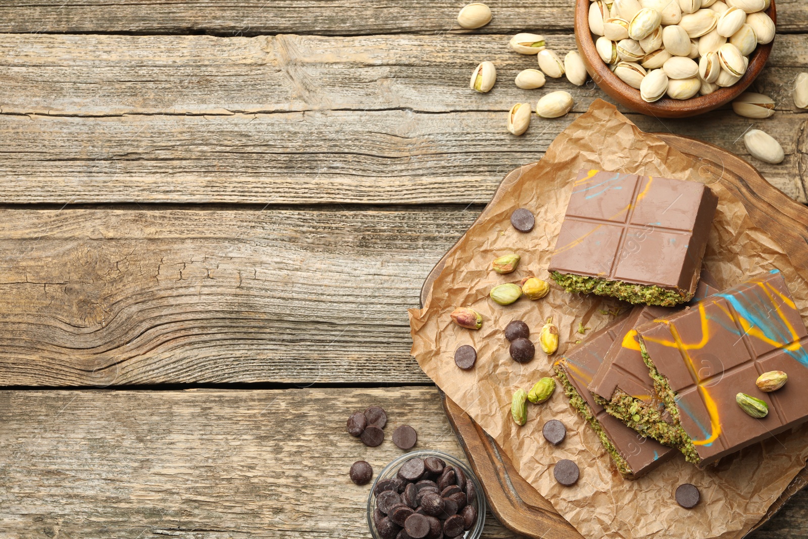 Photo of Pieces of Dubai chocolate bars with pistachios, knafeh and cacao chips on wooden table, flat lay. Space for text