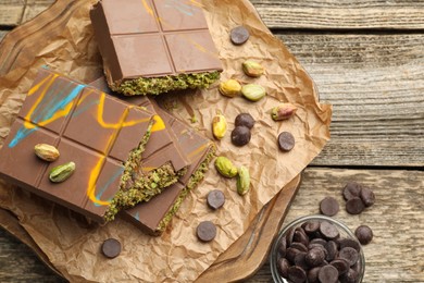 Photo of Pieces of Dubai chocolate bars with pistachios, knafeh and cacao chips on wooden table, flat lay