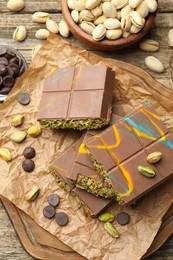 Photo of Pieces of Dubai chocolate bars with pistachios, knafeh and cacao chips on wooden table, flat lay