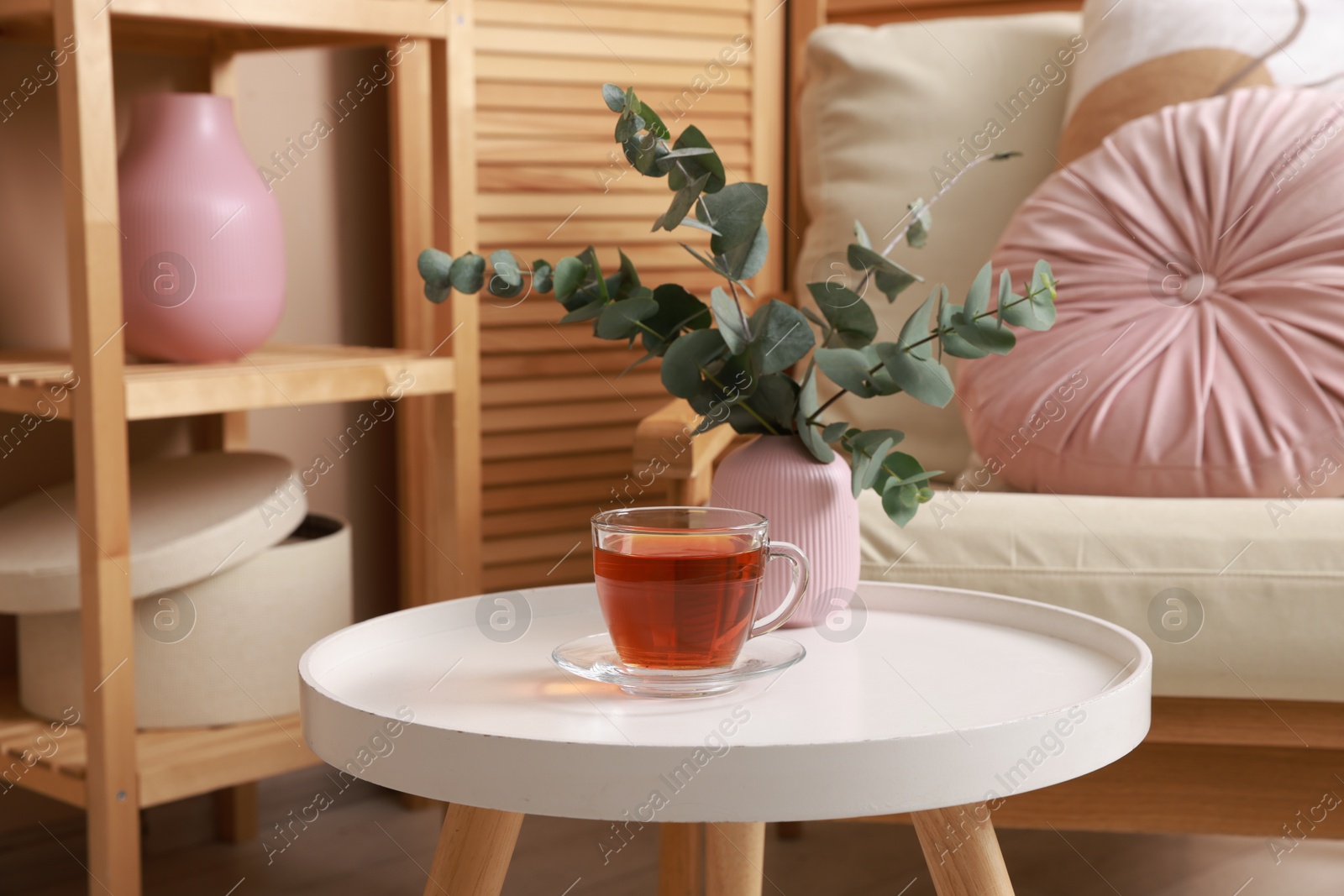 Photo of Coffee table with tea and eucalyptus near armchair at home