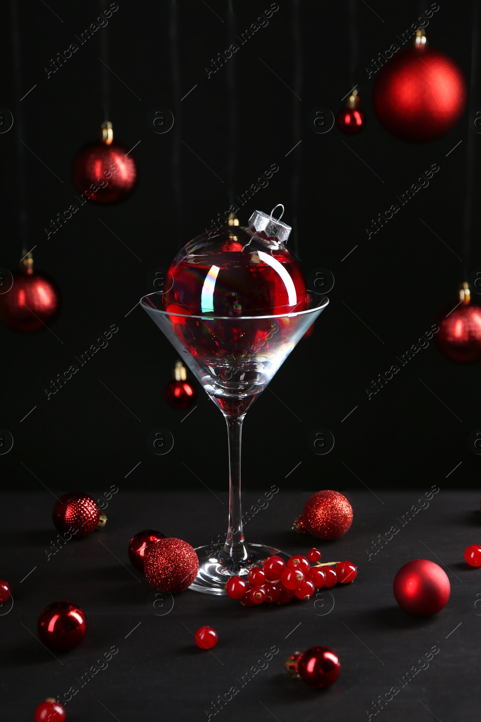 Photo of Creative presentation of Christmas cocktail in bauble and glass on black table