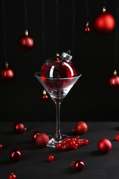 Photo of Creative presentation of Christmas cocktail in bauble and glass on black table