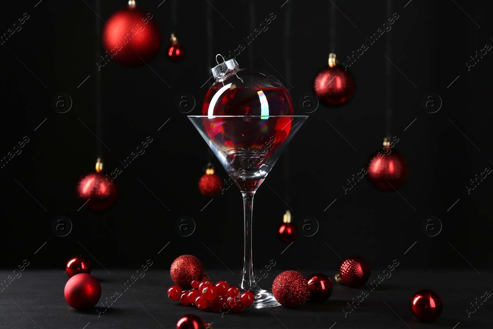 Photo of Creative presentation of Christmas cocktail in bauble and glass on black table