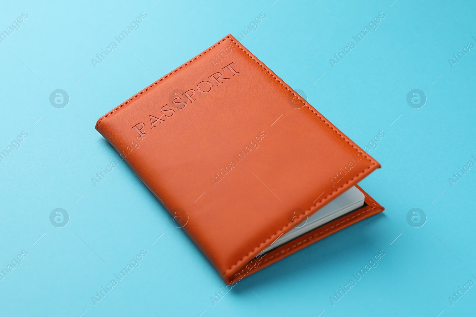 Photo of Passport in orange cover on light blue background, closeup