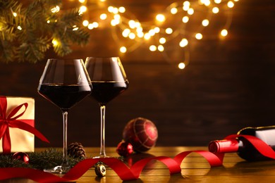 Photo of Red wine and beautiful Christmas decor on wooden table against blurred festive lights. Space for text