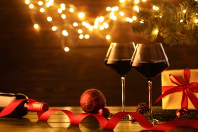 Photo of Red wine and beautiful Christmas decor on wooden table against blurred festive lights. Space for text