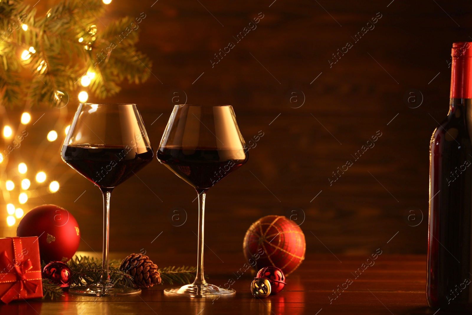 Photo of Red wine and beautiful Christmas decor on wooden table against blurred festive lights. Space for text