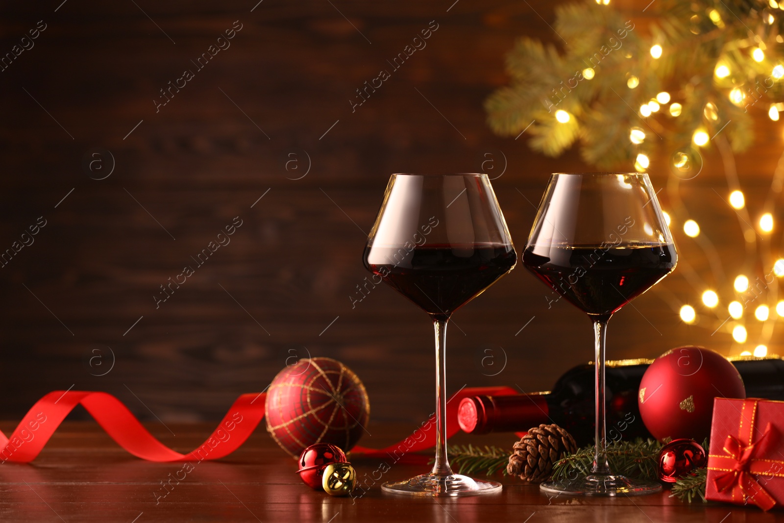 Photo of Red wine and beautiful Christmas decor on wooden table against blurred festive lights. Space for text