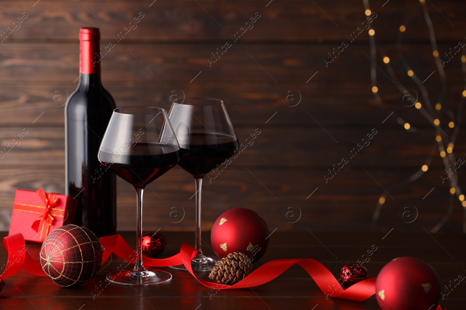 Photo of Red wine and beautiful Christmas decor on wooden table against blurred festive lights. Space for text