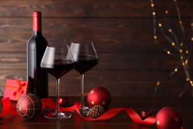 Photo of Red wine and beautiful Christmas decor on wooden table against blurred festive lights. Space for text