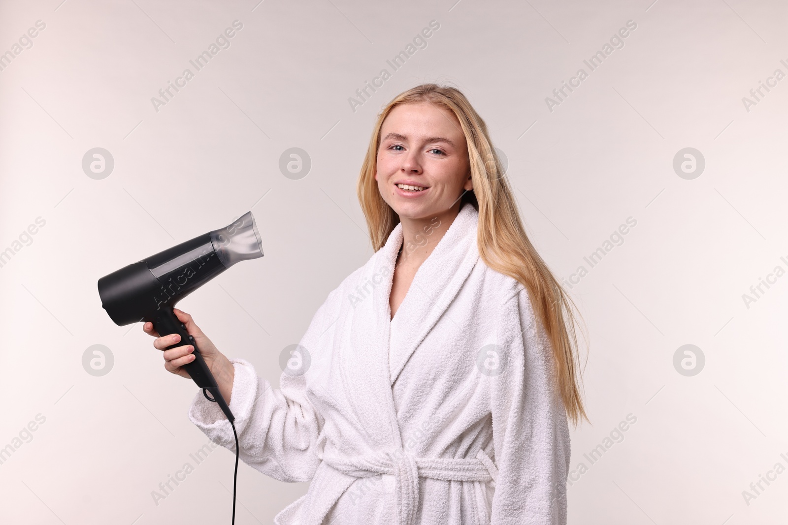 Photo of Beautiful young woman drying her hair with hairdryer on light grey background