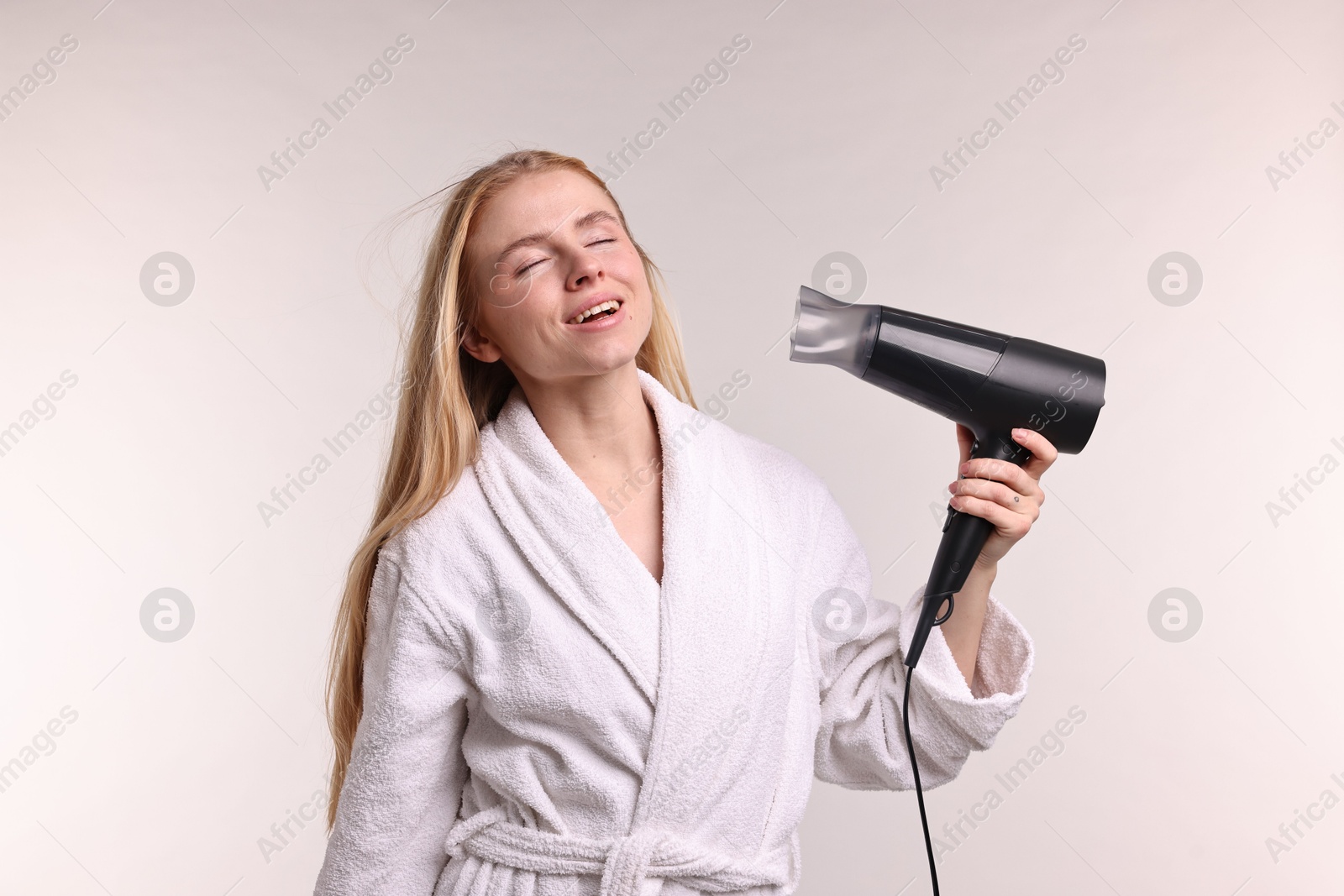 Photo of Beautiful young woman drying her hair with hairdryer on light grey background