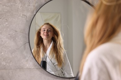 Photo of Beautiful young woman drying her hair near mirror in bathroom