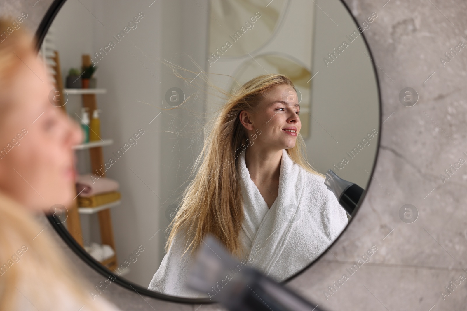 Photo of Beautiful young woman drying her hair near mirror in bathroom