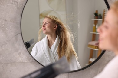 Photo of Beautiful young woman drying her hair near mirror in bathroom