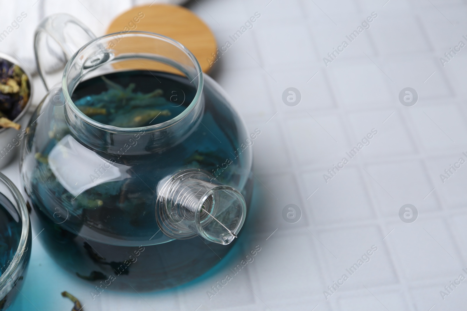 Photo of Delicious butterfly pea flower tea on white tiled table, closeup. Space for text