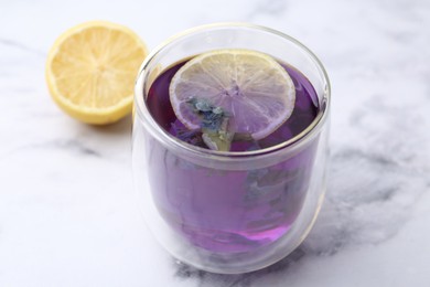 Delicious butterfly pea flower tea with lemon on white marble table, closeup