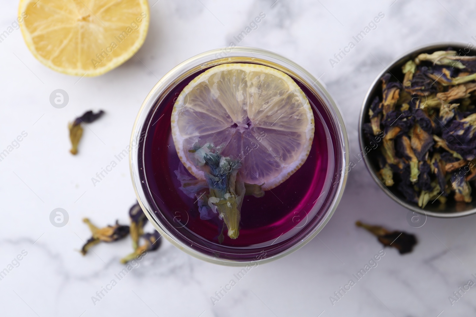 Photo of Delicious butterfly pea flower tea with lemon on white marble table, flat lay