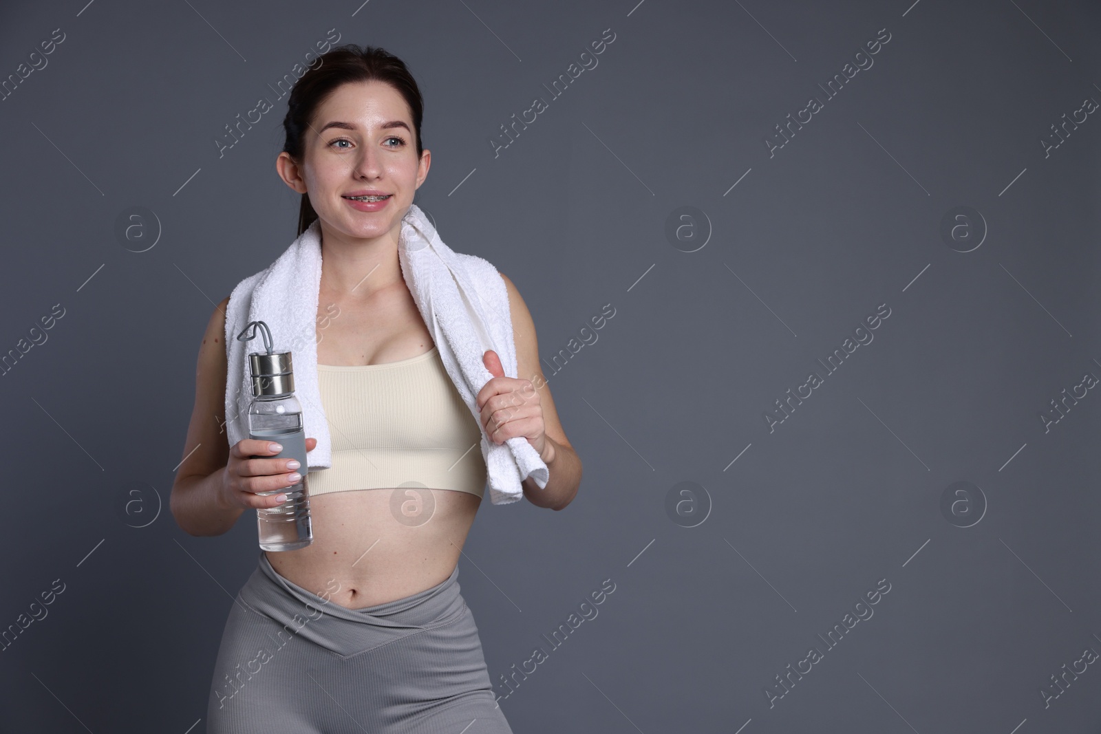 Photo of Woman in sportswear with bottle of water and towel on grey background, space for text