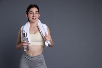 Photo of Woman in sportswear with bottle of water and towel on grey background, space for text