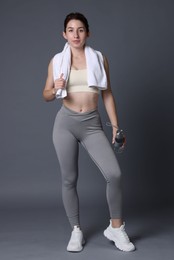 Photo of Woman in sportswear with bottle of water and towel on grey background