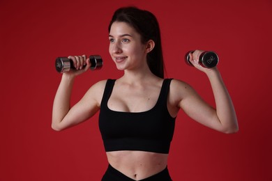 Photo of Woman in sportswear exercising with dumbbells on red background