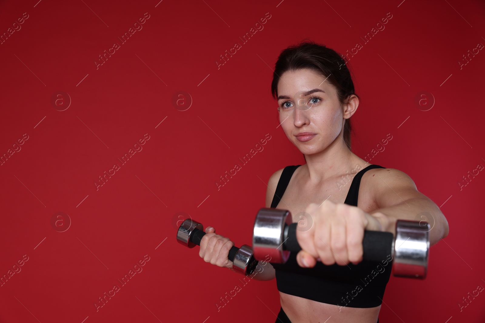 Photo of Woman in sportswear exercising with dumbbells on red background, space for text