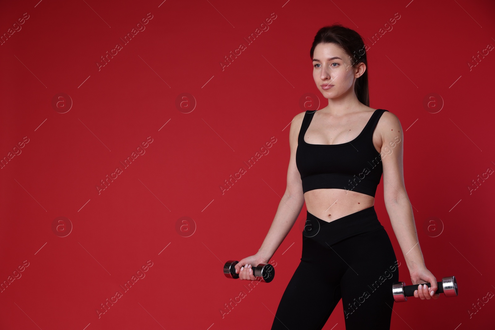 Photo of Woman in sportswear exercising with dumbbells on red background, space for text