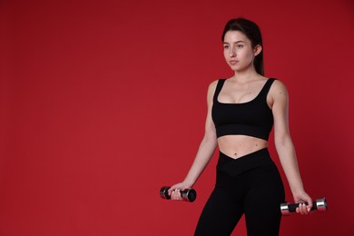 Woman in sportswear exercising with dumbbells on red background, space for text