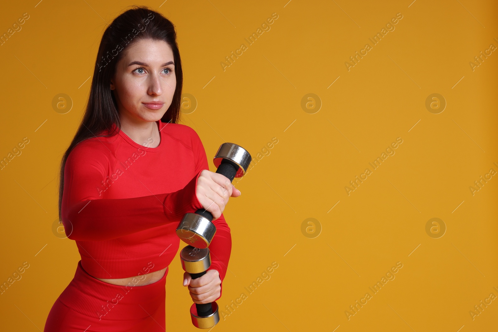 Photo of Woman in sportswear exercising with dumbbells on orange background, space for text