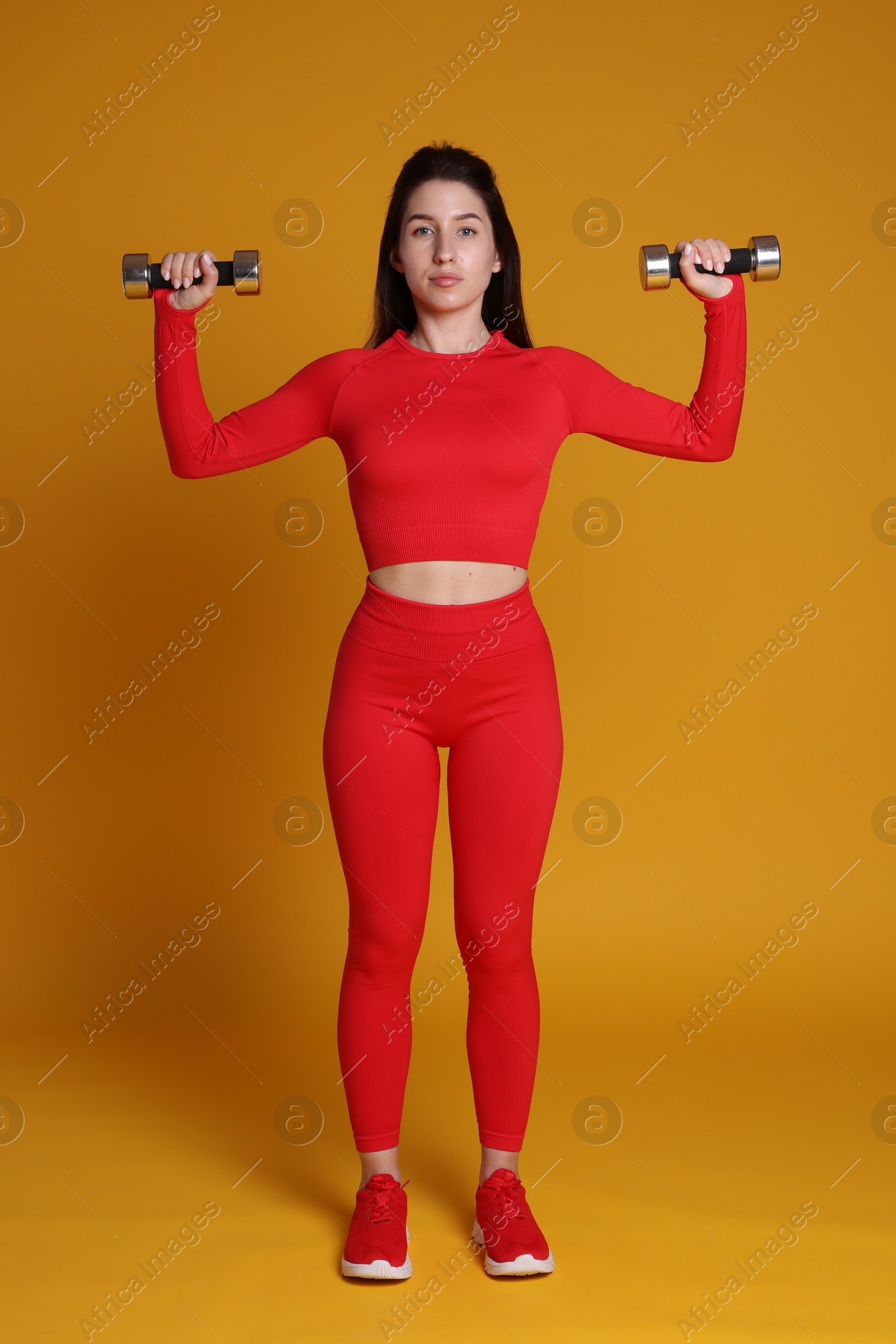 Photo of Woman in sportswear exercising with dumbbells on orange background