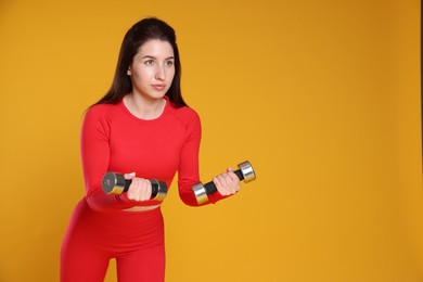 Photo of Woman in sportswear exercising with dumbbells on orange background, space for text