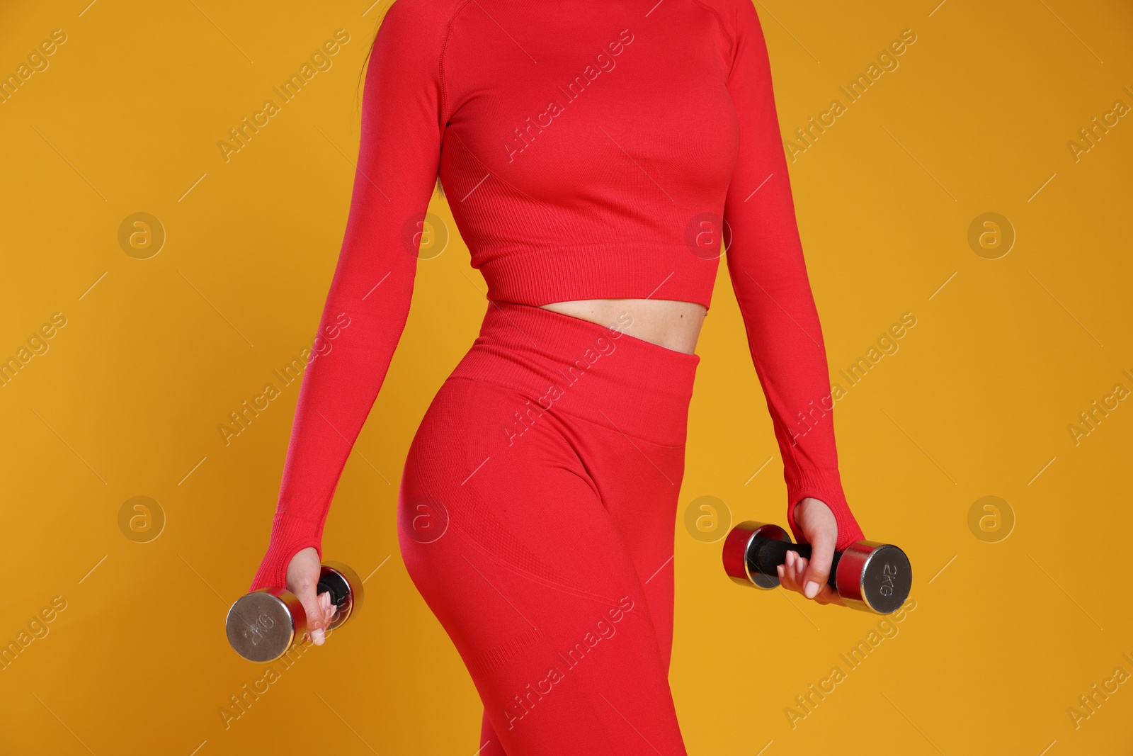 Photo of Woman in sportswear exercising with dumbbells on orange background, closeup