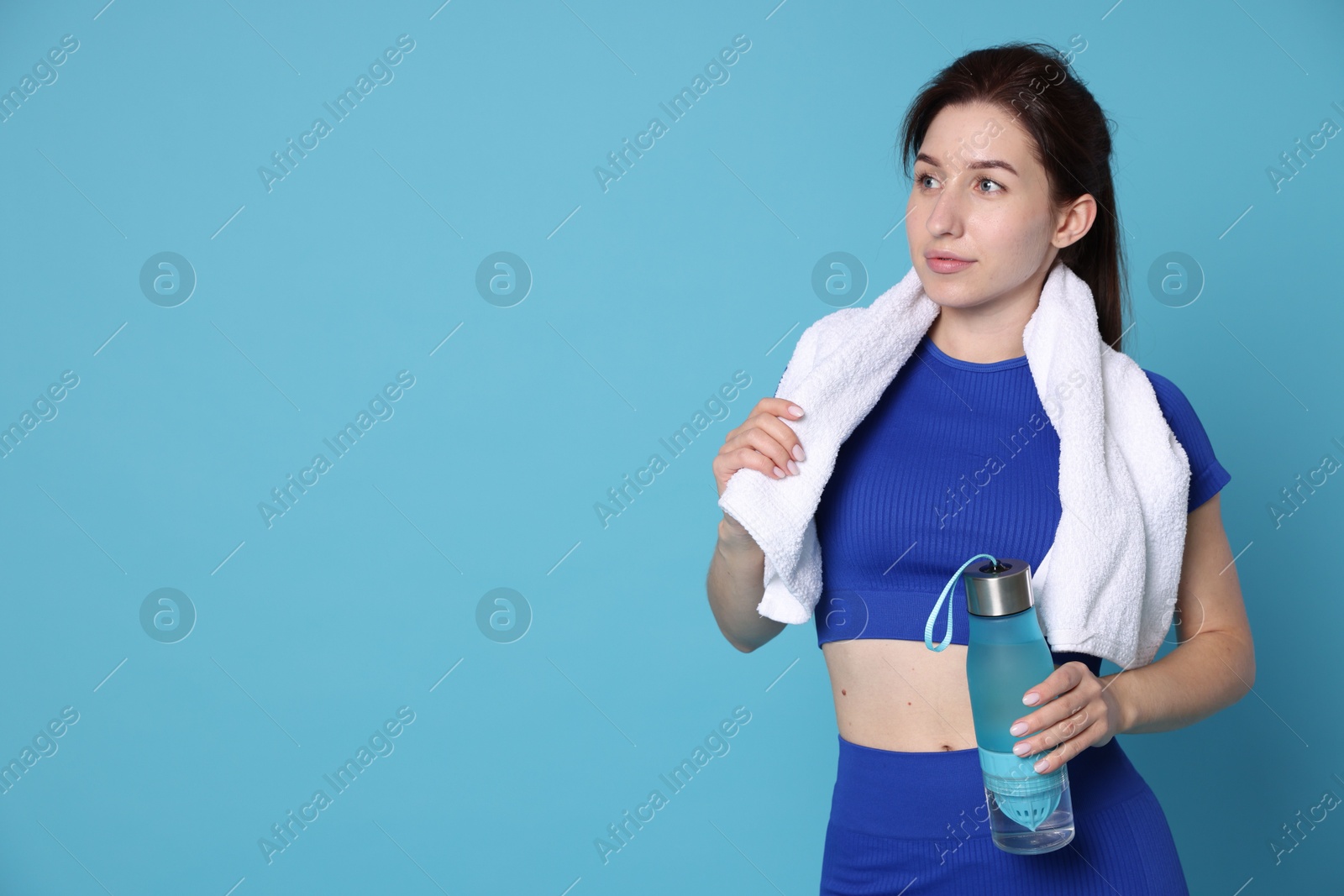 Photo of Woman in sportswear with bottle of water and towel on light blue background, space for text