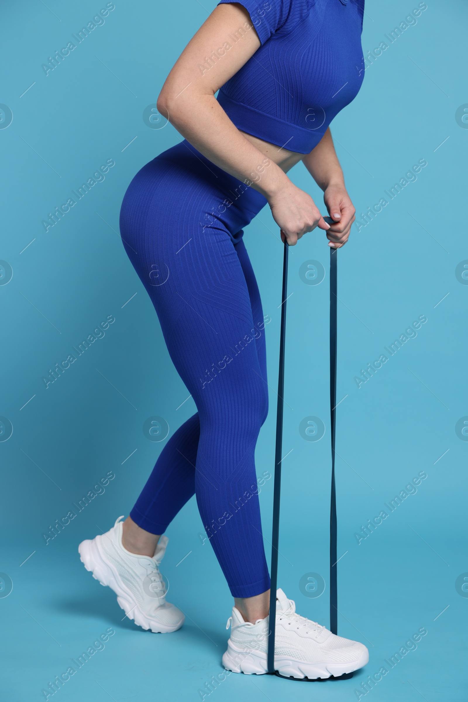 Photo of Woman in sportswear exercising elastic band on light blue background, closeup