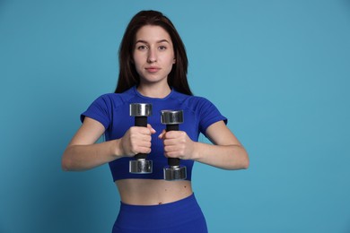 Photo of Woman in sportswear exercising with dumbbells on light blue background