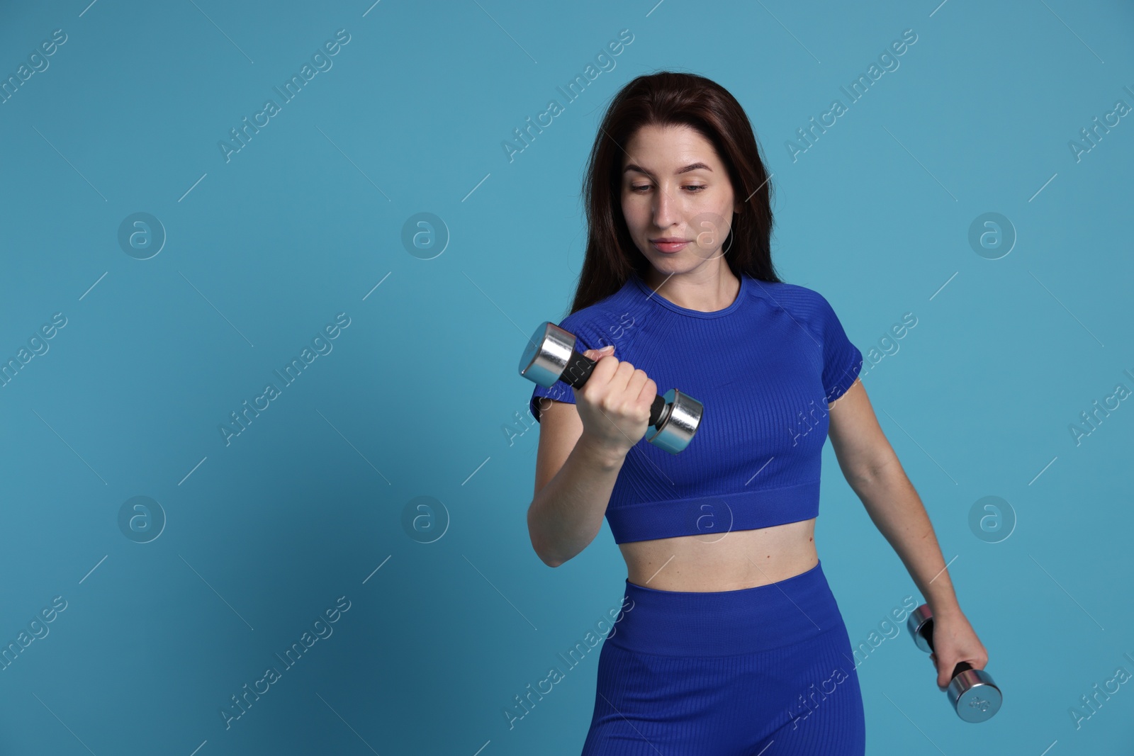 Photo of Woman in sportswear exercising with dumbbells on light blue background, space for text