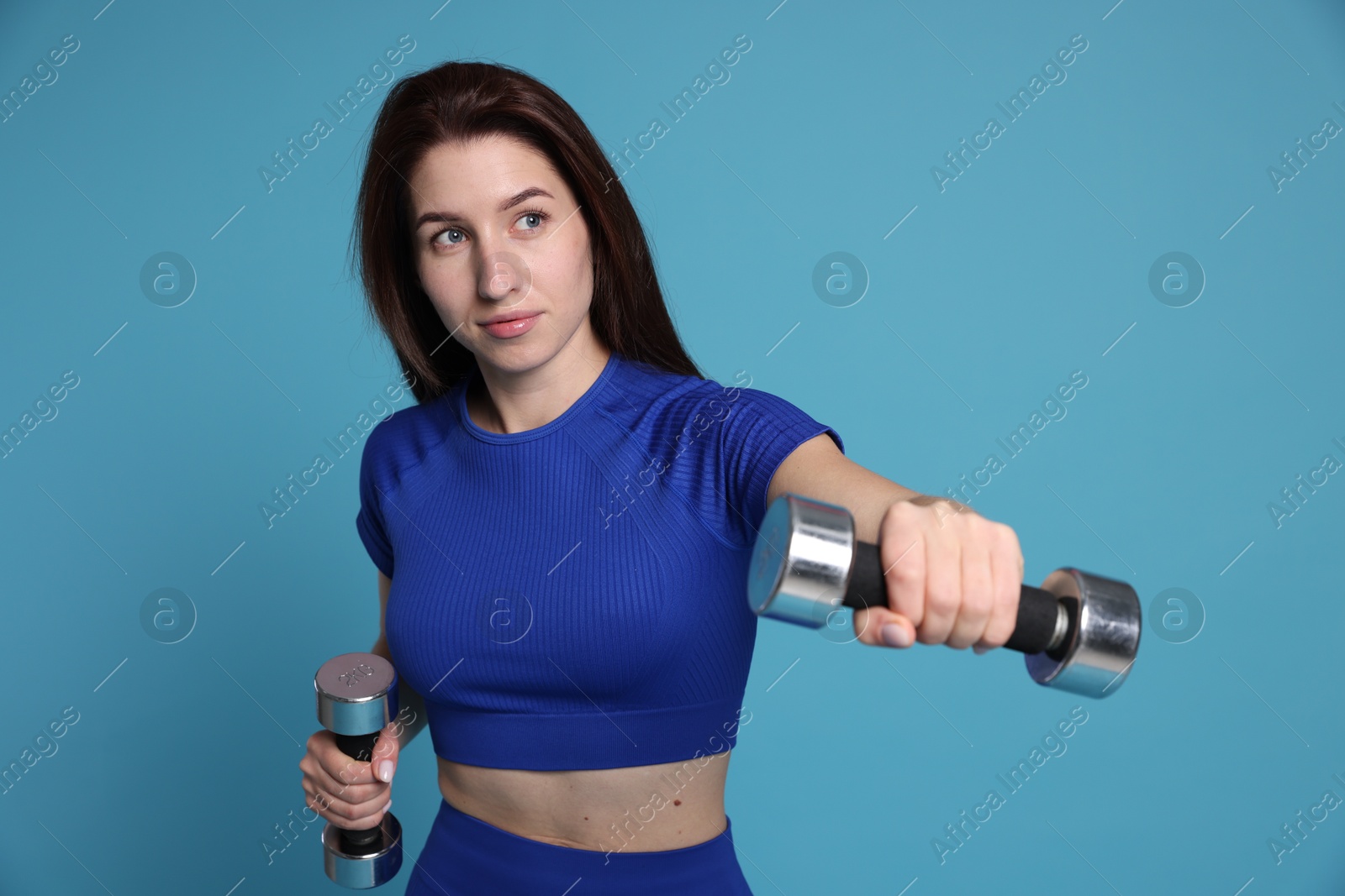 Photo of Woman in sportswear exercising with dumbbells on light blue background