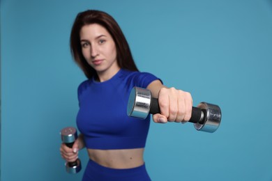 Photo of Woman in sportswear exercising with dumbbells on light blue background, selective focus