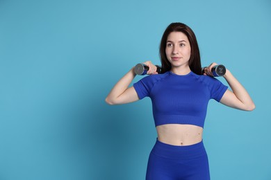 Photo of Woman in sportswear exercising with dumbbells on light blue background, space for text